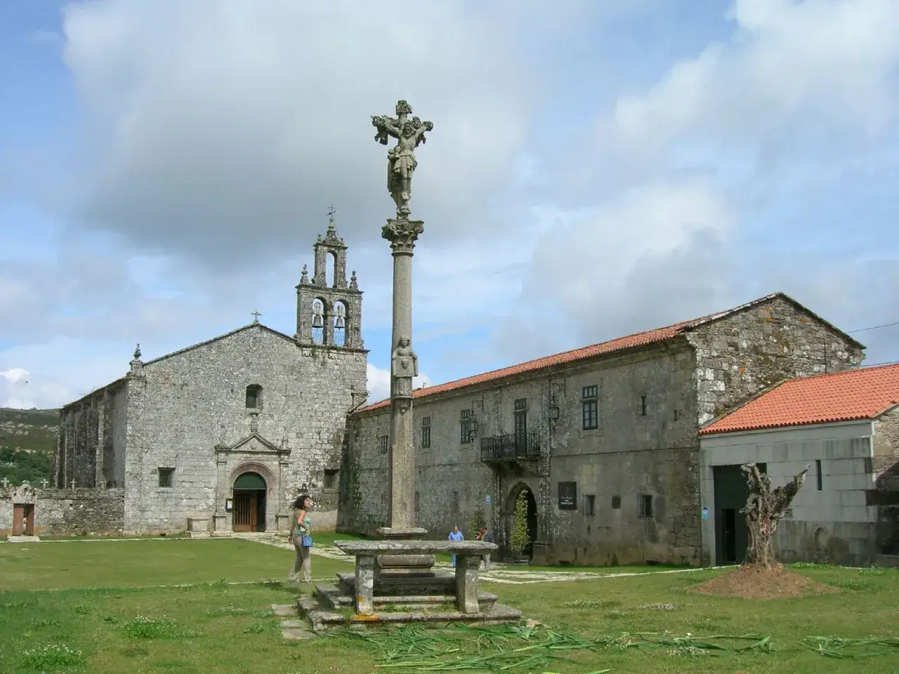 El monasterio de Aciveiro, con su iglesia de piedra y un cruceiro imponente, se alza bajo un cielo nublado.