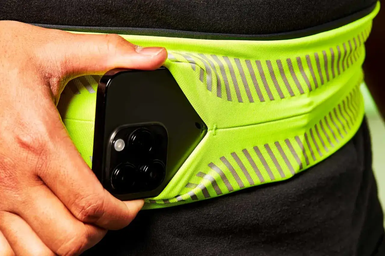 Hand wird in eine neongelbe Bauchtasche gesteckt, perfekt f&uuml;r das Handy beim Joggen. Reflektierende Streifen sorgen f&uuml;r Sichtbarkeit.