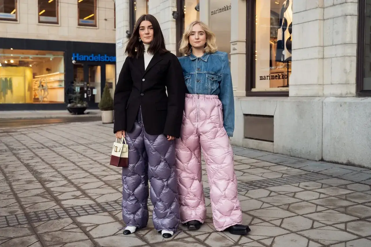 Due donne sfoggiano un audace abbinamento rosa e blu con pantaloni imbottiti oversize. Una porta un blazer nero, l'altra una giacca di jeans.