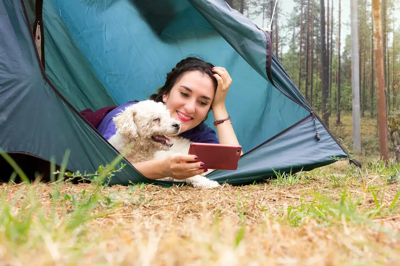 En kvinna och hennes hund myser i ett tält. De njuter av att campa med hund i skogen och tar en selfie.