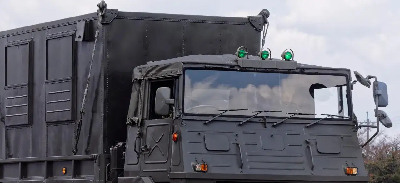 Camion militaire sombre avec trois gyrophares verts allum&eacute;s sur le toit. Le gyrophare vert signification peut varier, mais ici il signale une pr&eacute;sence discr&egrave;te.