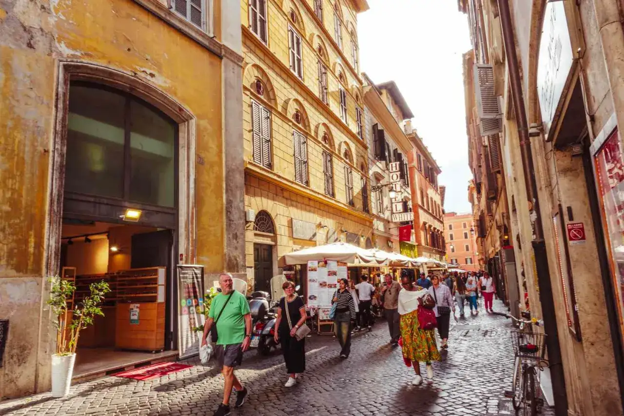 Une rue pavée animée à Rome, une destination européenne de rêve. Des bâtiments anciens, des terrasses de café et des passants créent une atmosphère vibrante.