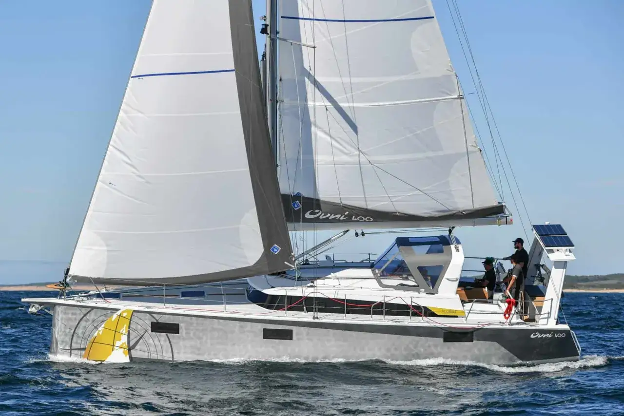 Un puro yacht a vela solca le onde con vele bianche gonfie. Tre persone a bordo godono della navigazione.