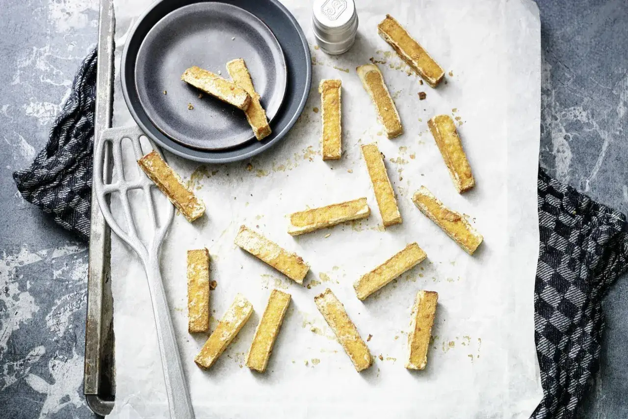 Goldbraun gebackenes **Tofu im Ofen**, verteilt auf Backpapier. Daneben ein Teller, ein Spatel und ein K&uuml;chentuch.