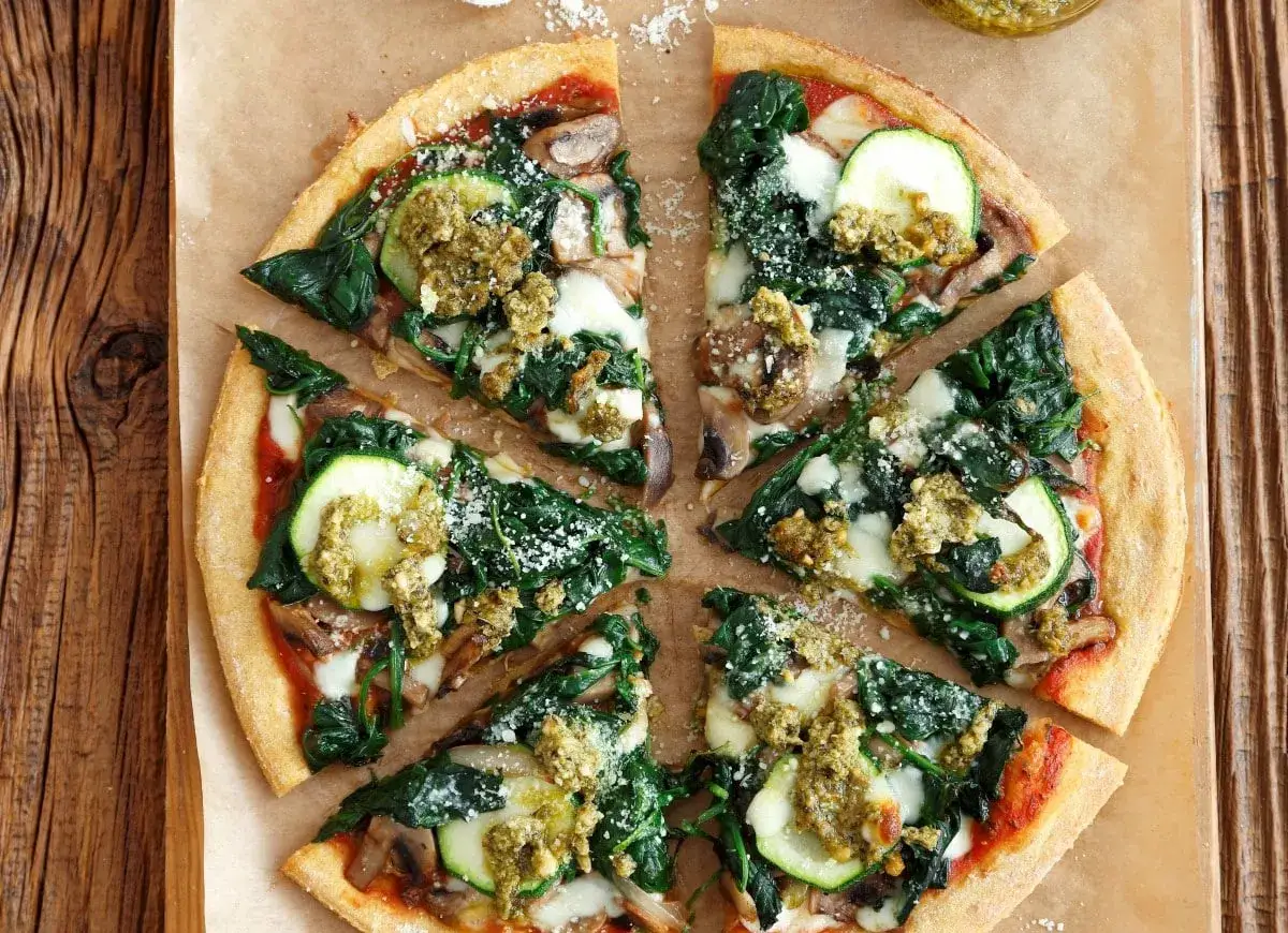 Pyszna pizza z fetą, szpinakiem, cukinią i pieczarkami, polana zielonym pesto.
