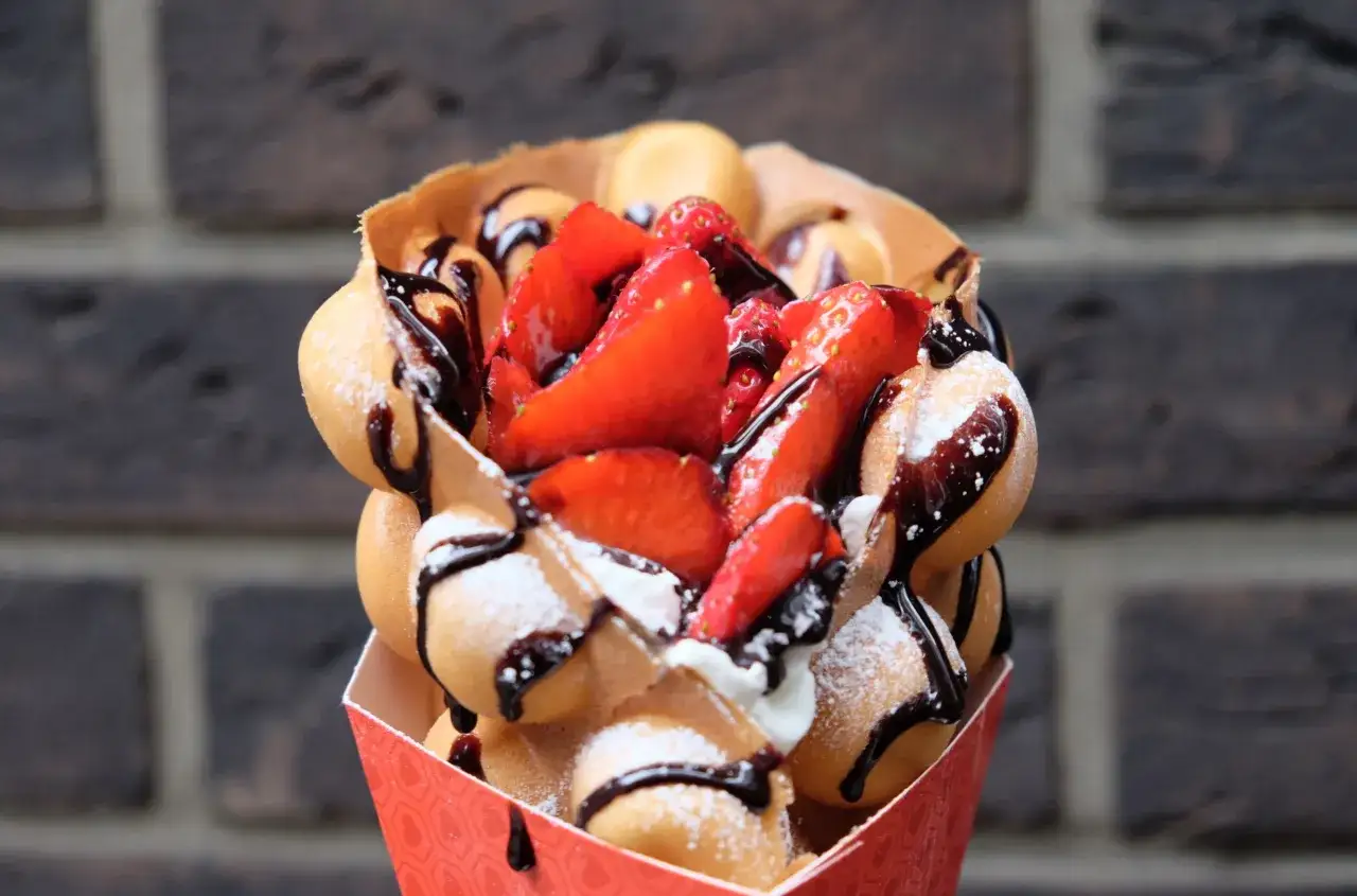 Ein köstliches Bubble Eis mit frischen Erdbeeren, Schokoladensauce und Puderzucker, serviert in einem roten Papierbehälter.