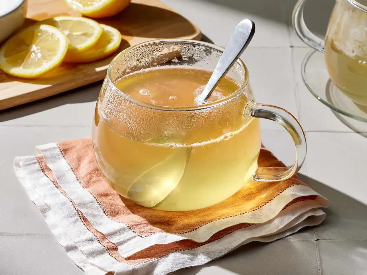 Une tasse de boisson eau et miel fumante, avec des rondelles de citron sur une planche à découper en arrière-plan.