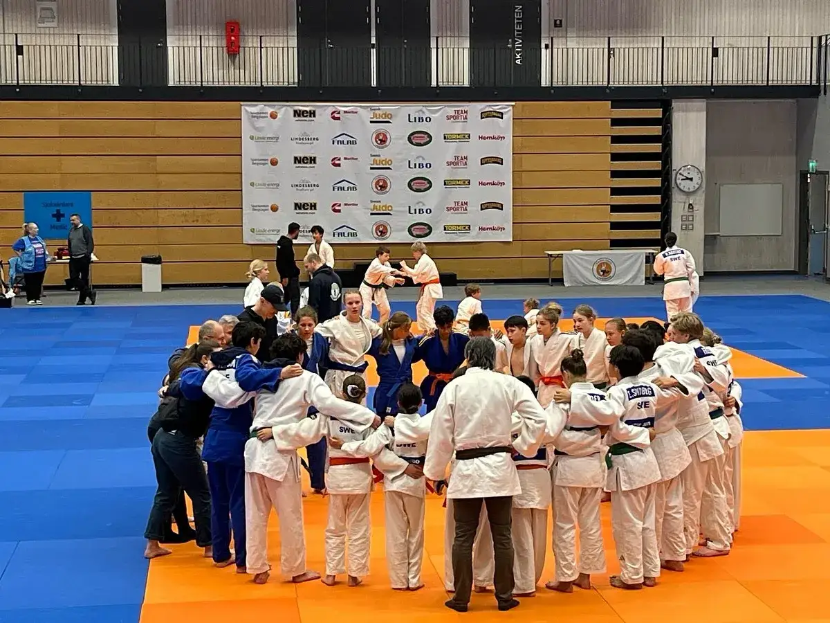 Barn och vuxna i judodr&auml;kter st&aring;r i en ring p&aring; en judomatta. Kanske &auml;r det Marcus Nyman som tr&auml;nar dem.