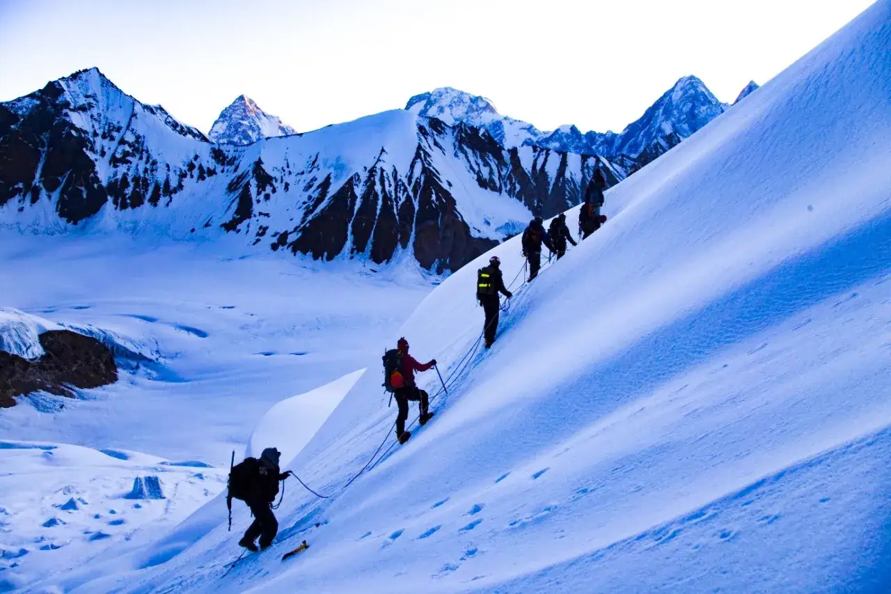 Grupa alpinistów wspina się po ośnieżonym zboczu w kierunku szerokiego szczytu.