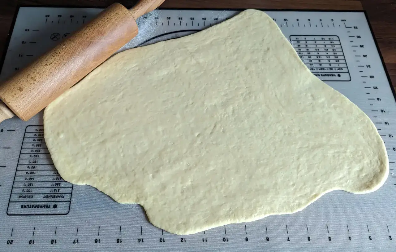 P&acirc;te &agrave; beignet &eacute;tal&eacute;e sur un tapis de mesure, avec un rouleau &agrave; p&acirc;tisserie en bois.
