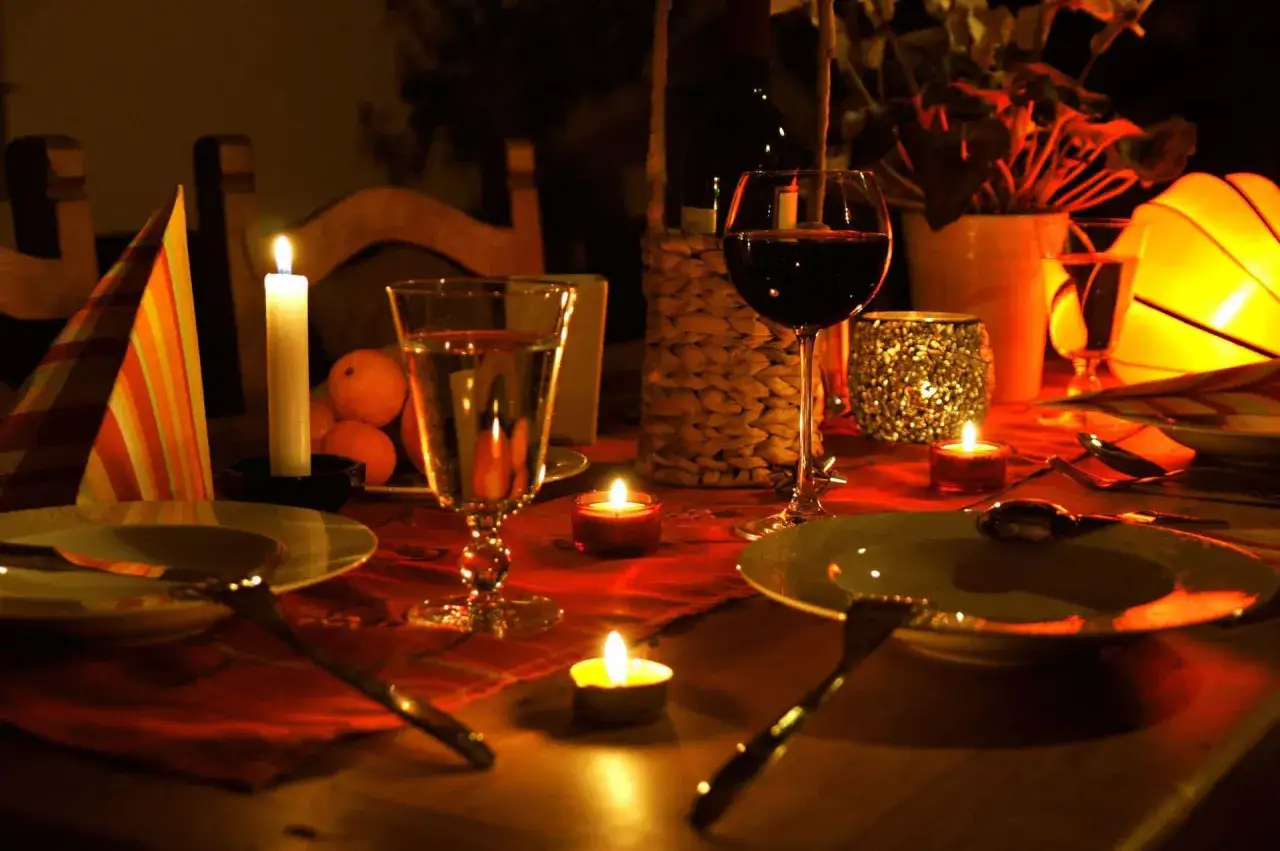 Romantyczna kolacja dla dwojga przy blasku świec. Na stole wino, kieliszki, owoce i nakrycia.