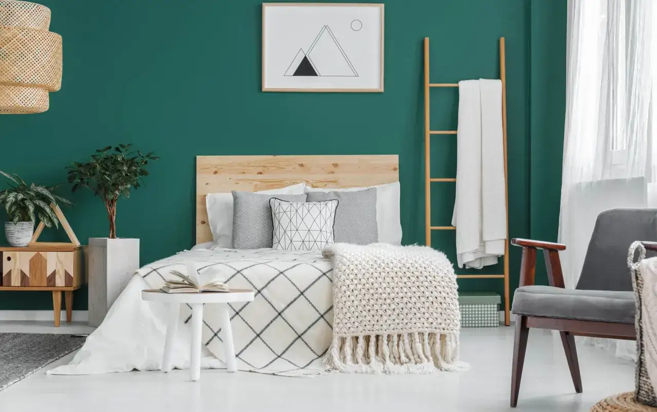 Un letto accogliente con coperta a trama grossa e cuscini geometrici, circondato da piante e un quadro astratto. Un esempio di camere da letto belle e rilassanti.