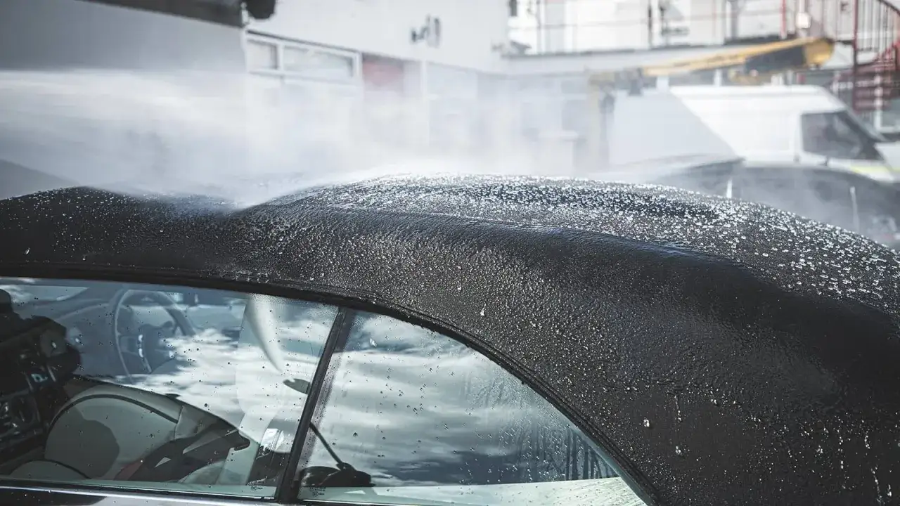 Czyszczenie dachu cabrio pod strumieniem wody. Krople deszczu odbijają się od czarnego materiału, tworząc błyszczącą powierzchnię.