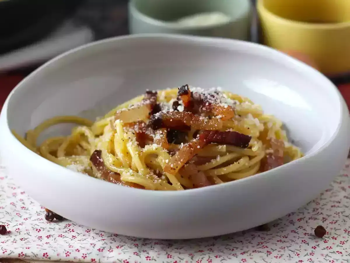 Pyszne spaghetti carbonara, jak zrobić sos carbonara bez śmietany zgodnie z włoską tradycją. Danie posypane parmezanem i guanciale.