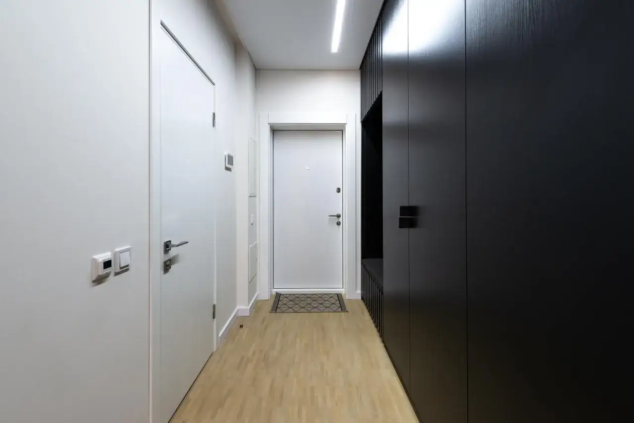 Pasillo largo y estrecho con paredes blancas y un armario negro. Ideas para decorar paredes como decorar un pasillo largo y estrecho.
