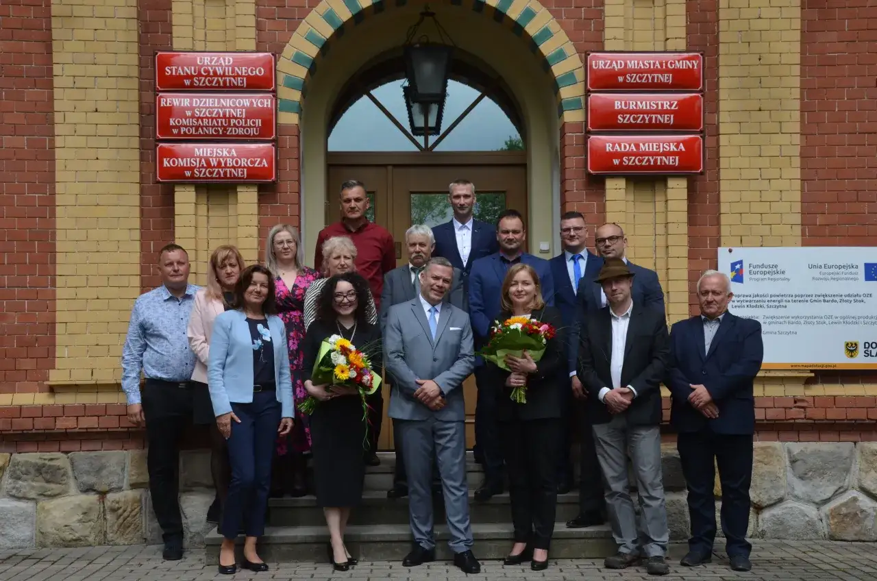 Grupa osób przed budynkiem urzędu, gdzie widnieje tablica