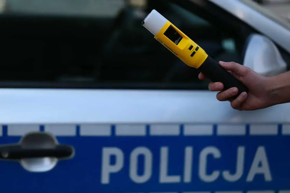 Ręka trzyma żółty alkomat. Na samochodzie napis POLICJA. Wynik 0,13 promila w wydychanym powietrzu.