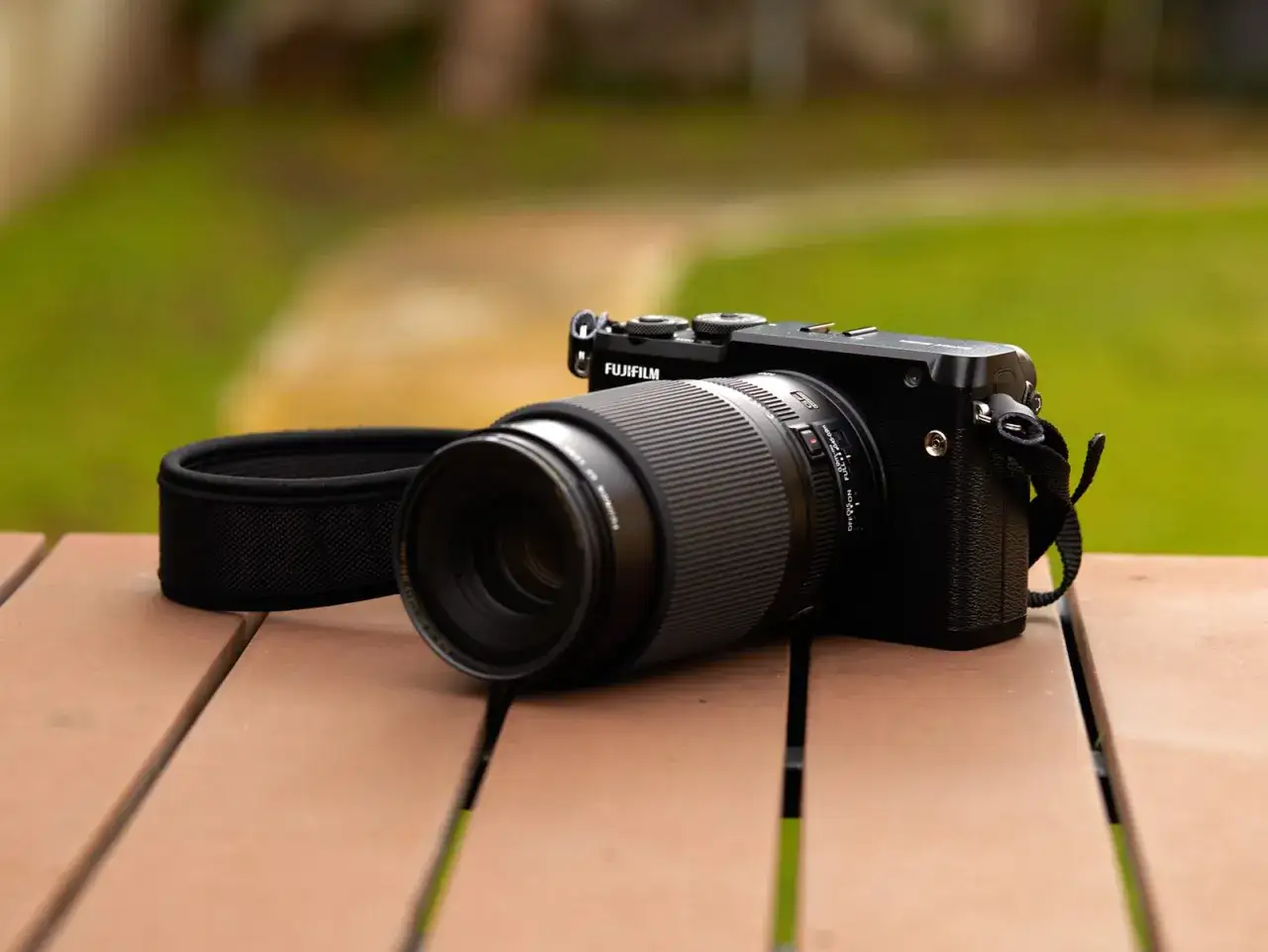 C&aacute;mara Fujifilm GFX 50R con lente en mesa de madera, lista para capturar la belleza del exterior.