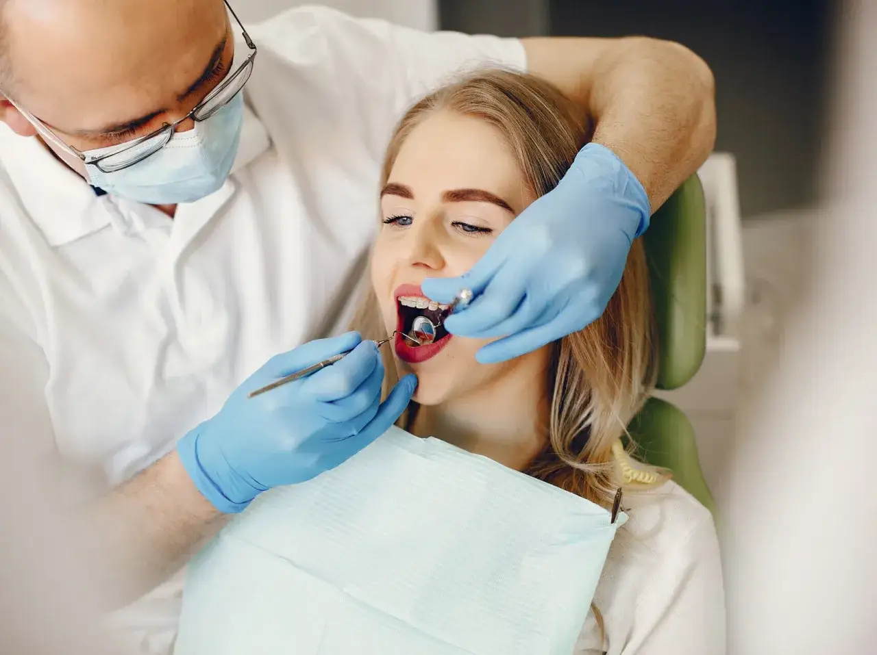 Dentysta w niebieskich rękawiczkach wykonuje zabieg piłowania zębów u młodej kobiety.