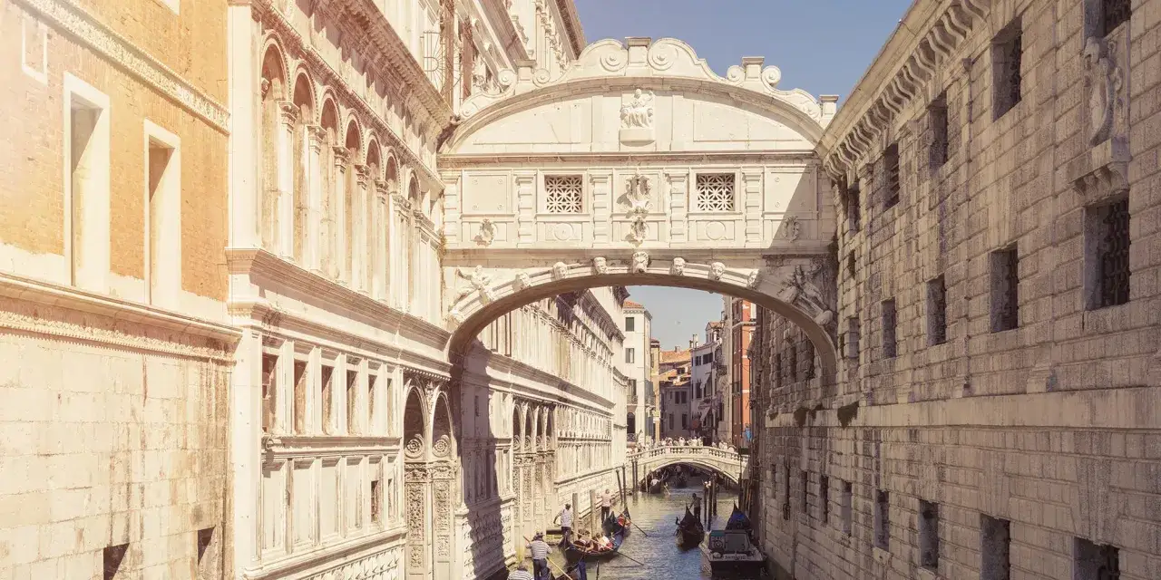 Il Ponte dei Sospiri, avvolto dalla sua leggenda, collega il Palazzo Ducale alle prigioni. Gondole scivolano sul canale sottostante.
