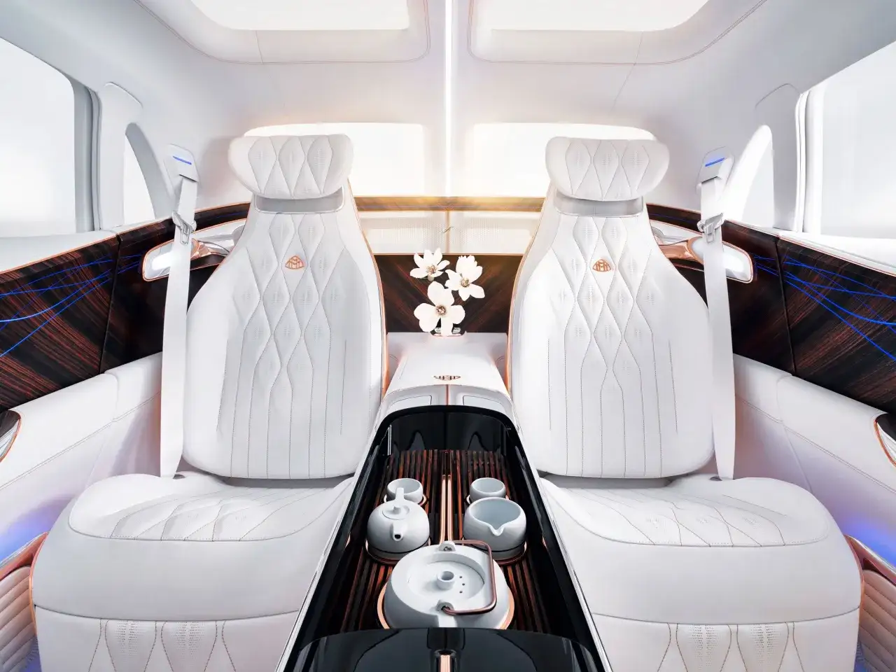 Luksusowe wnętrze Maybach SUV z białymi, pikowanymi fotelami, drewnianymi panelami i zestawem do herbaty.