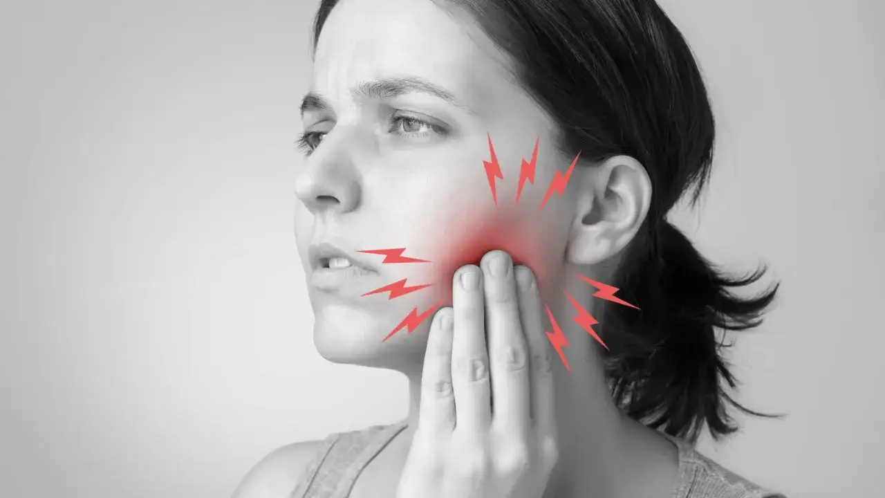 Mujer con dolor de muelas, toc&aacute;ndose la mejilla. Rayos rojos indican la zona afectada. &iquest;Qu&eacute; hacer para el dolor de muelas?