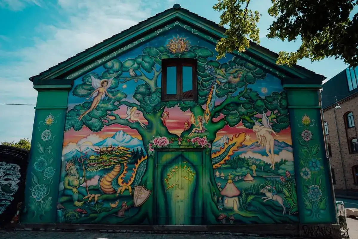 Freetown Christiania: bajkowy mural na ścianie budynku z latającymi wróżkami, smokiem i baśniową krainą.