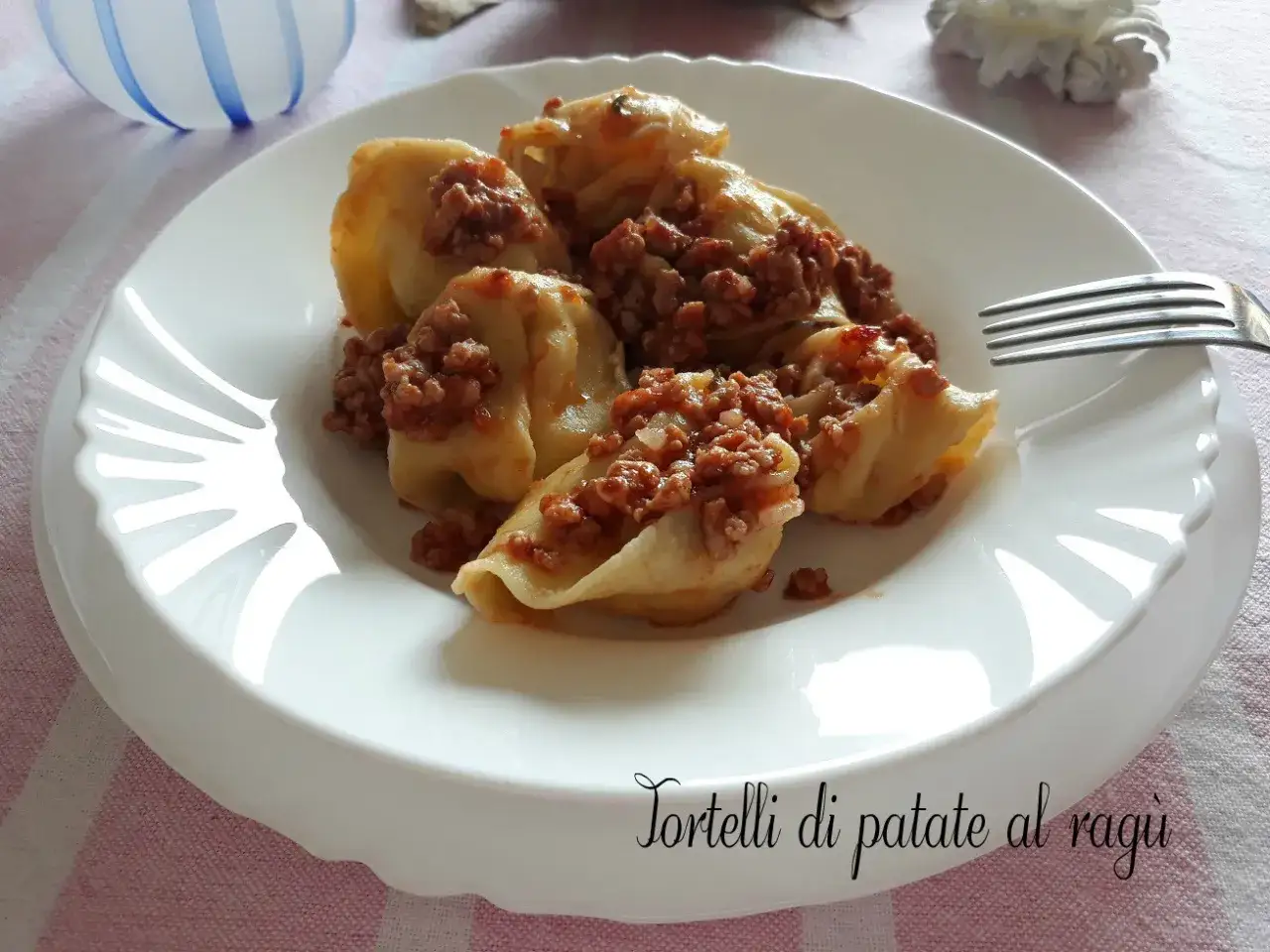 Tortelli di patate al ragù, un piatto gustoso e confortante, servito su un piatto bianco con una forchetta pronta.