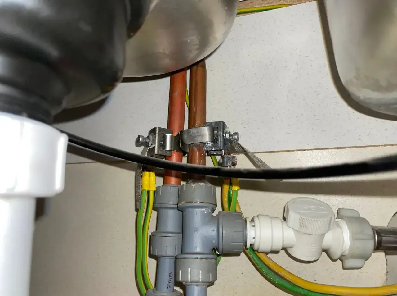 Connexion de mise &agrave; la terre sur tuyau cuivre sous un &eacute;vier. Des fils verts et jaunes sont fix&eacute;s aux tuyaux pour assurer la s&eacute;curit&eacute; &eacute;lectrique.