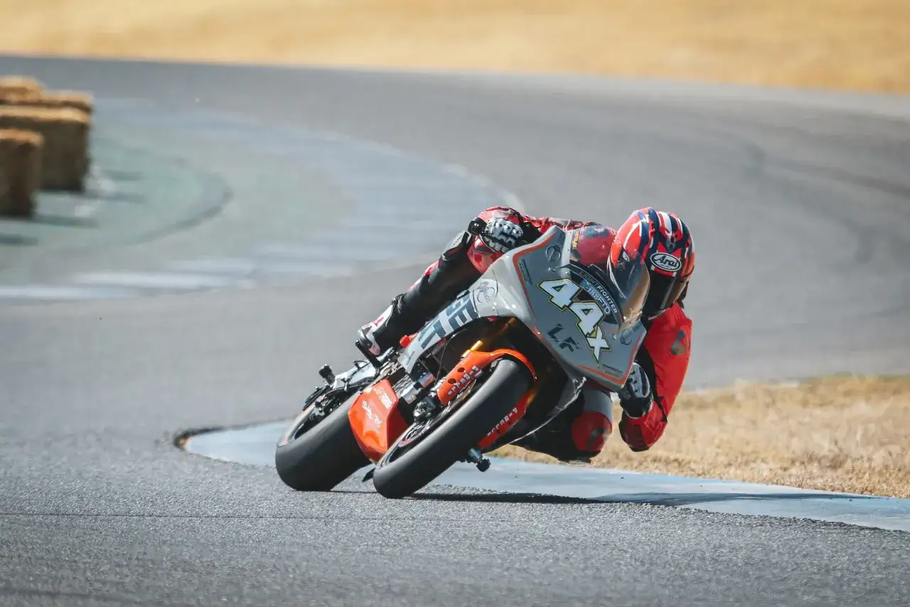 Piloto en moto de carreras, modelo Lightning LS-218, inclinado en curva.
