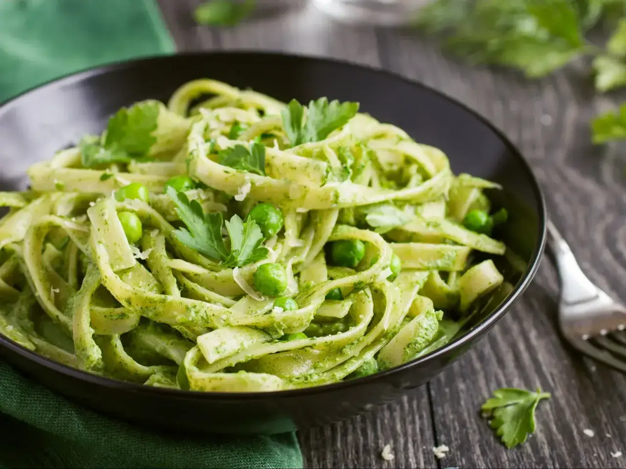 Talerz pełen makaronu z pesto, groszku i listków pietruszki. Danie wygląda apetycznie i świeżo.