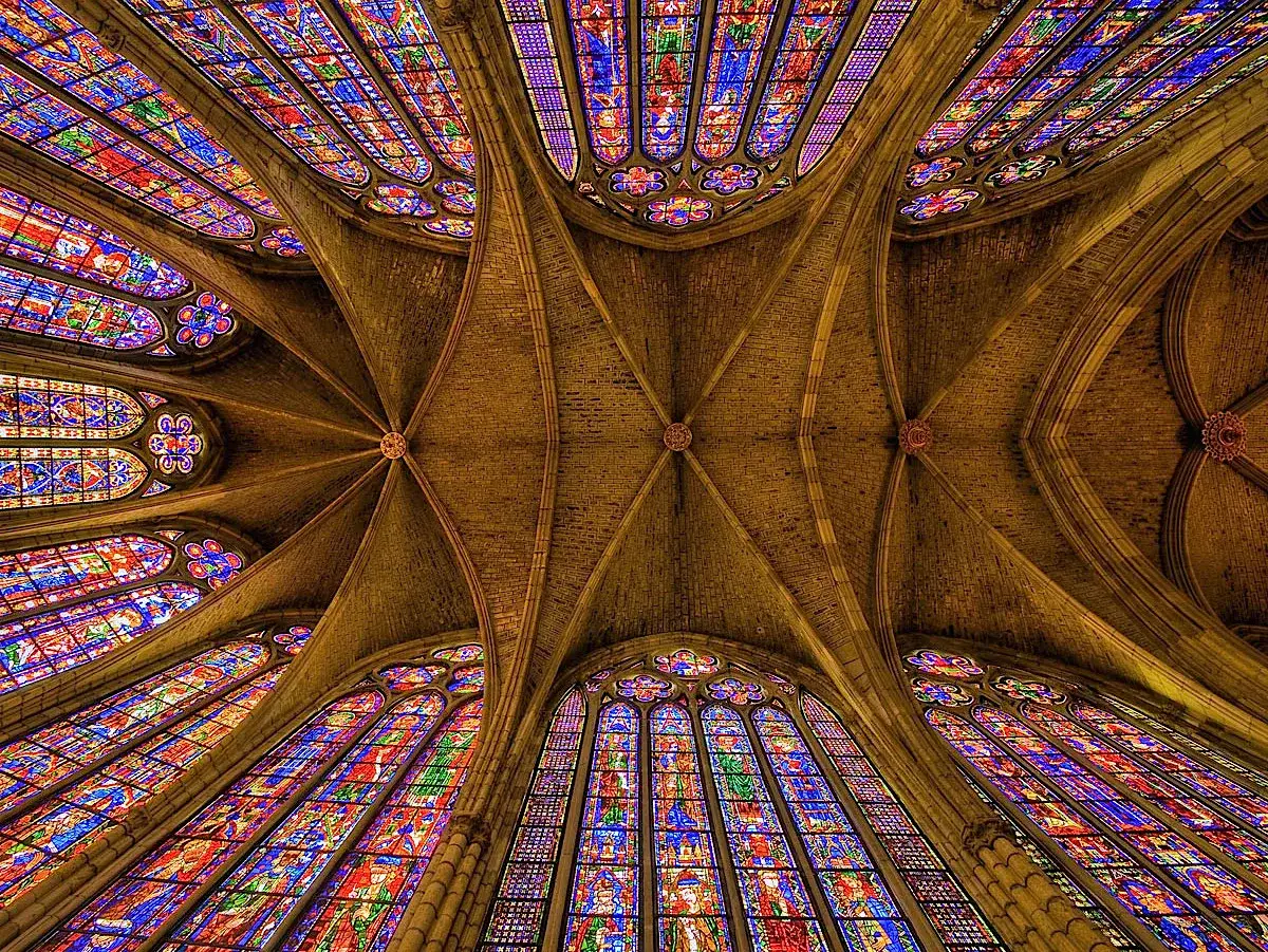 Techo abovedado de una catedral gótica, con vidrieras de colores vibrantes que iluminan el espacio. Las **arte gótico características** de arcos apuntados y bóvedas de crucería son evidentes.