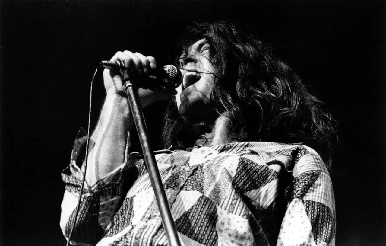 Charyzmatyczny wokalista Deep Purple z długimi włosami, śpiewający z pasją do mikrofonu.
