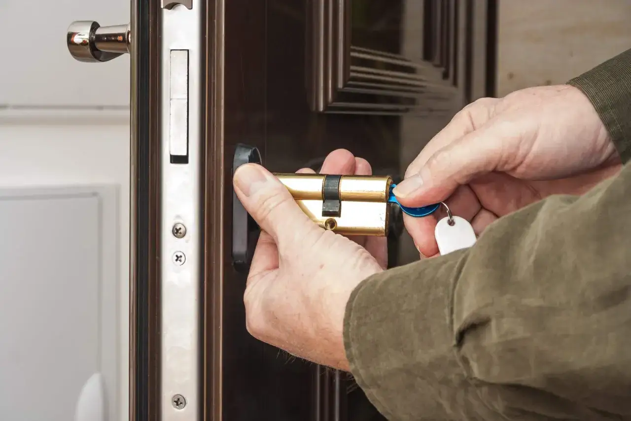 Mains tenant un cylindre de serrure en laiton et une cl&eacute; bleue pour changer la serrure d'une porte.