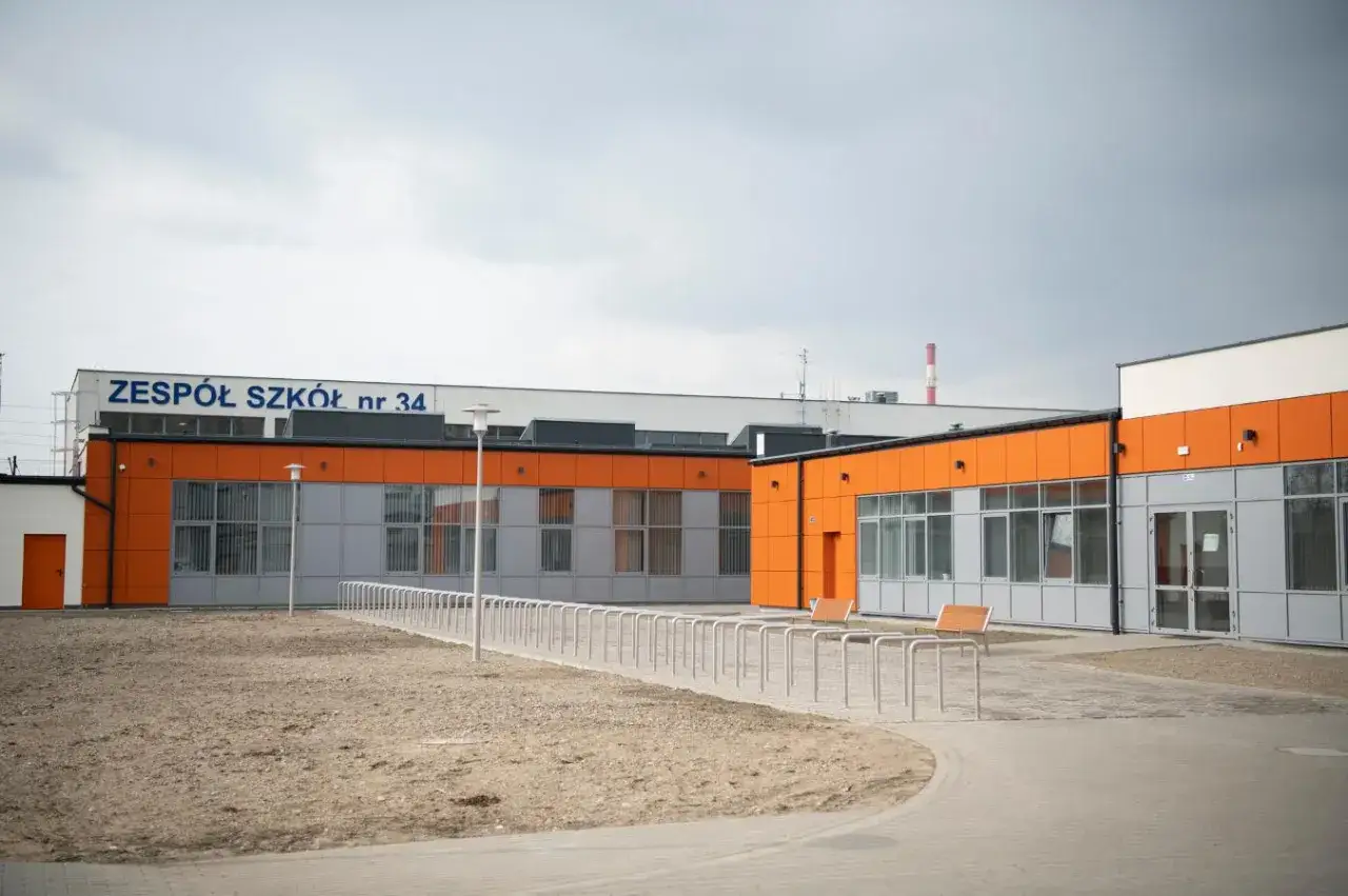 Nowoczesny budynek Zespołu Szkół nr 34 w Warszawie, z pomarańczowymi akcentami. To miejsce, gdzie młodzi artyści rozwijają swoje talenty.
