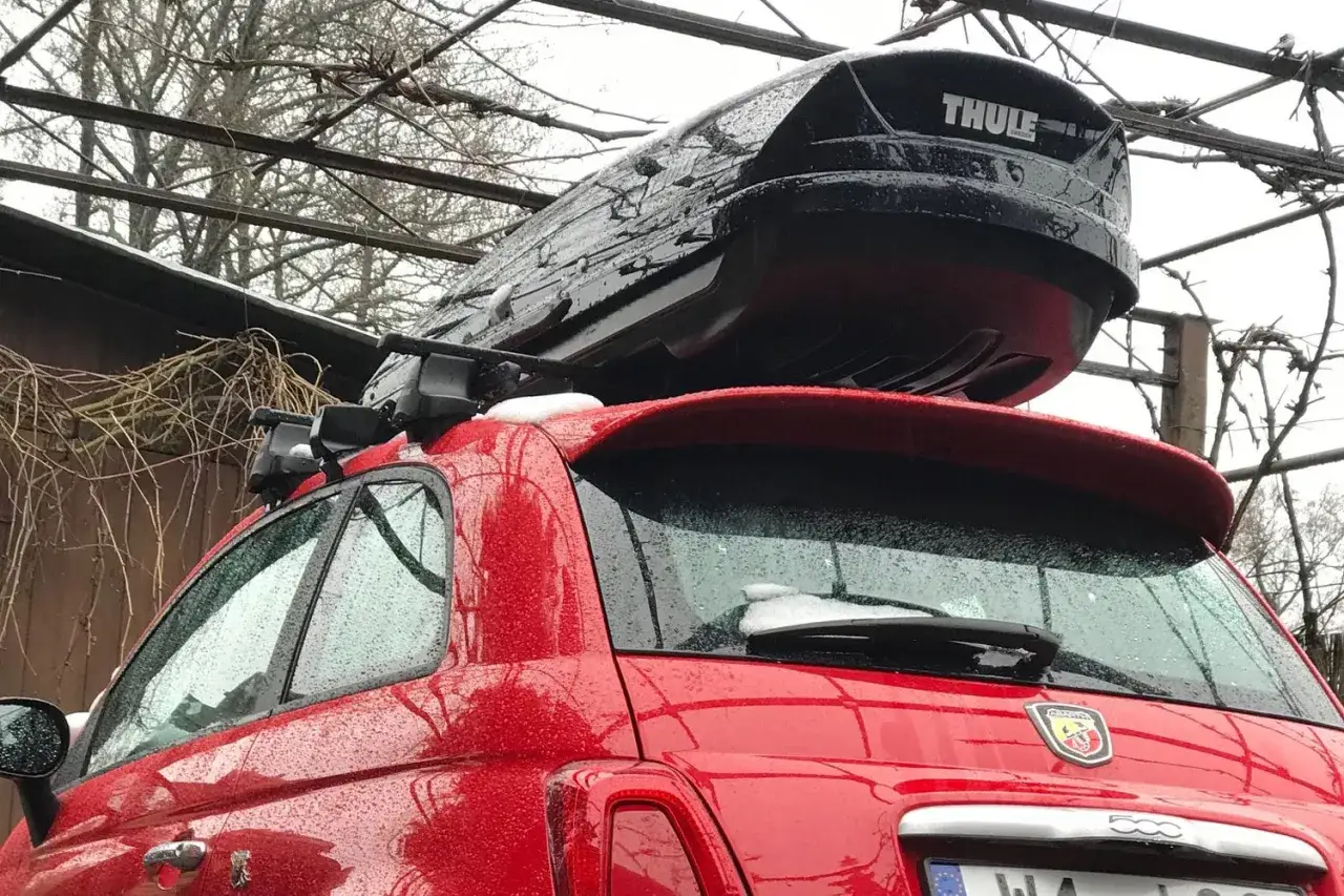 Czerwony Fiat 500 z boxem dachowym Thule, gotowy do przewożenia nart w samochodzie.