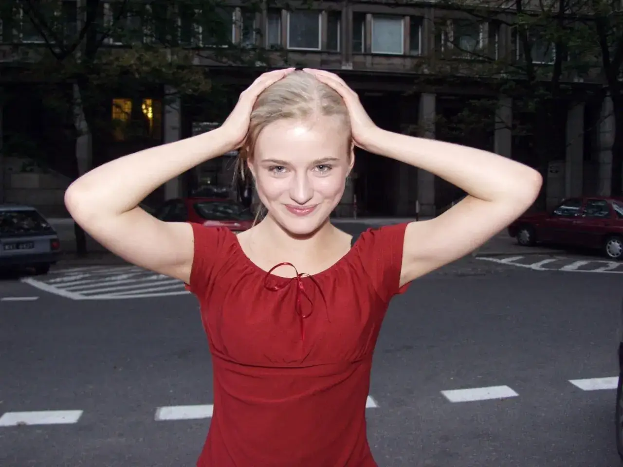Marta Chodorowska z uśmiechem, ręce na głowie. W tle budynek i samochody.