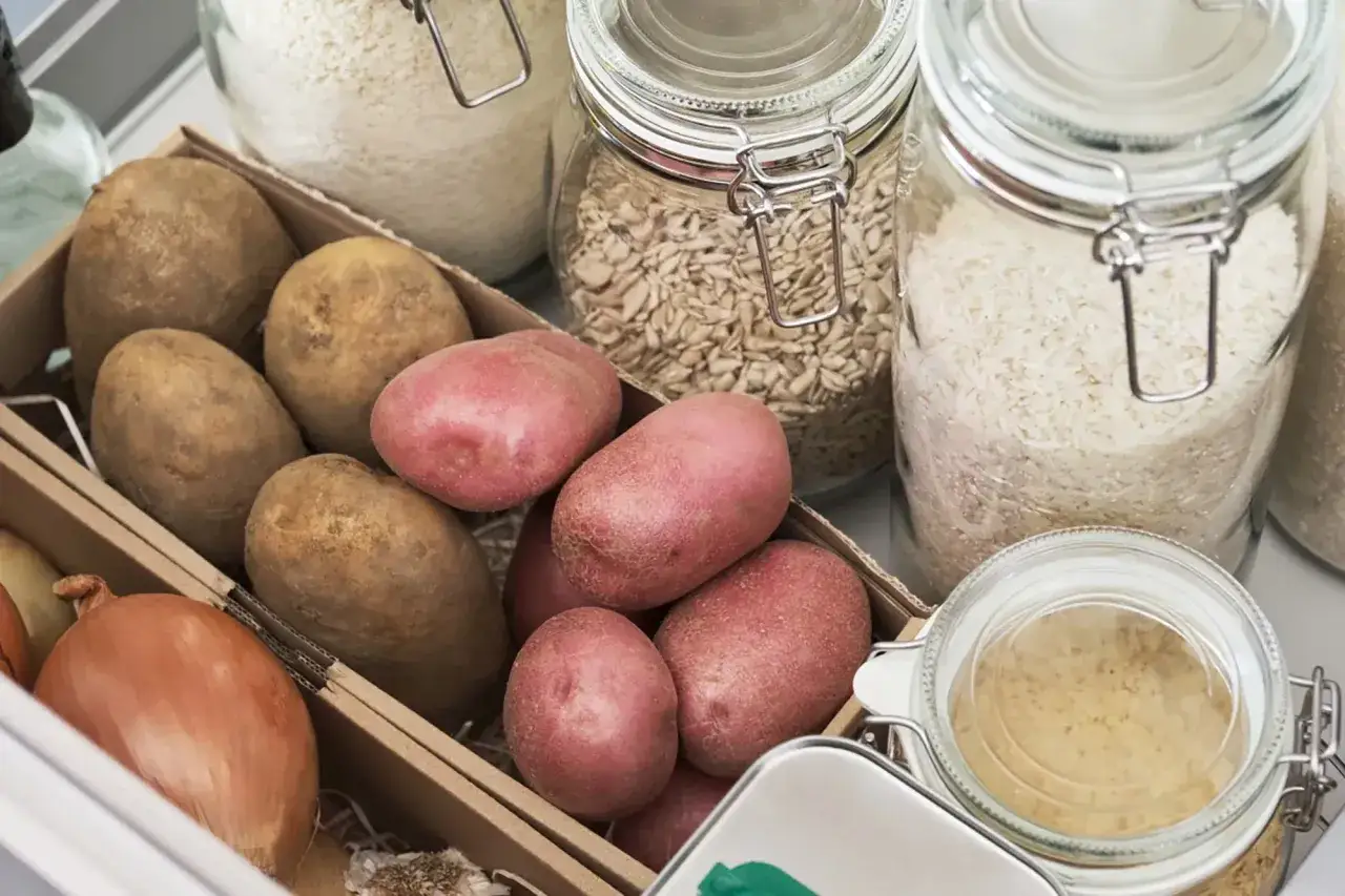 Kartoffeln lagern ohne Keller: Eine Kiste mit Kartoffeln und Zwiebeln neben Gl&auml;sern mit Reis und Haferflocken.