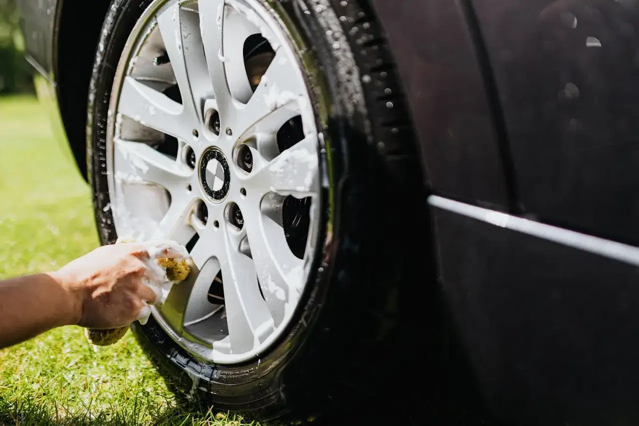 Mycie felg domowe sposoby: ręka ze gąbką czyści spienioną felgę BMW na trawie.