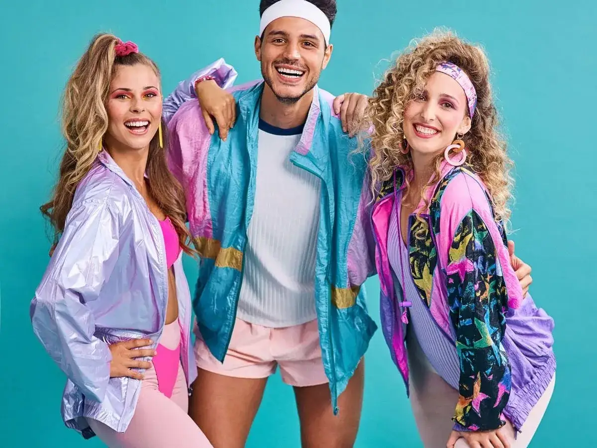 Trzy osoby w kolorowych strojach sportowych, z burzą loków i kucykiem, emanują energią lat 80. styl.