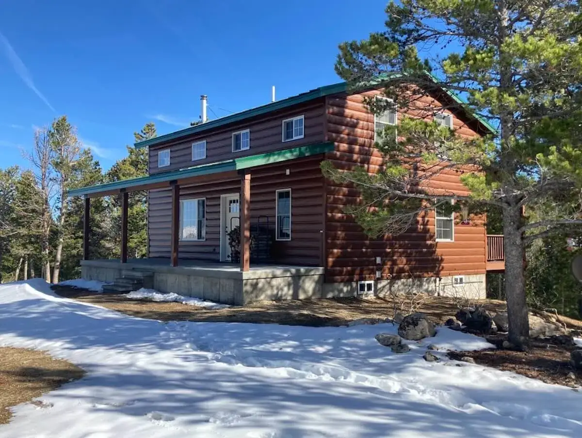 A cozy log cabin with a covered porch sits in a snowy landscape, ready for winter. Learn how to winterize your home to keep it warm and safe.