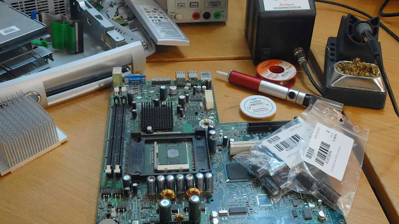 Computerplatine mit CPU, RAM-Slots und vielen Kondensatoren. Werkzeuge zum Löten und Ersatzteile liegen bereit. Mögliche Symptome eines kondensator defekt sind hier zu sehen.