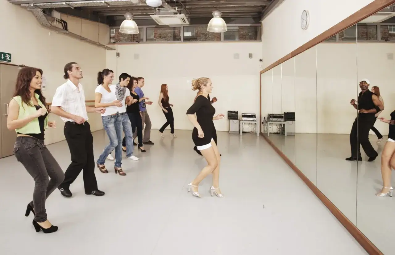 Grupa osób na kursie instruktora tańca ćwiczy ruchy przed lustrem.