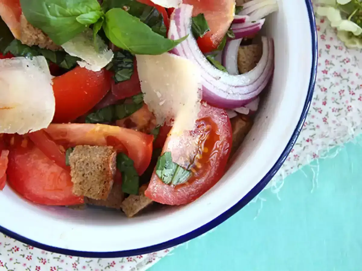 En närbild på en läcker italiensk sallad med tomater, rödlök, basilika och parmesan.