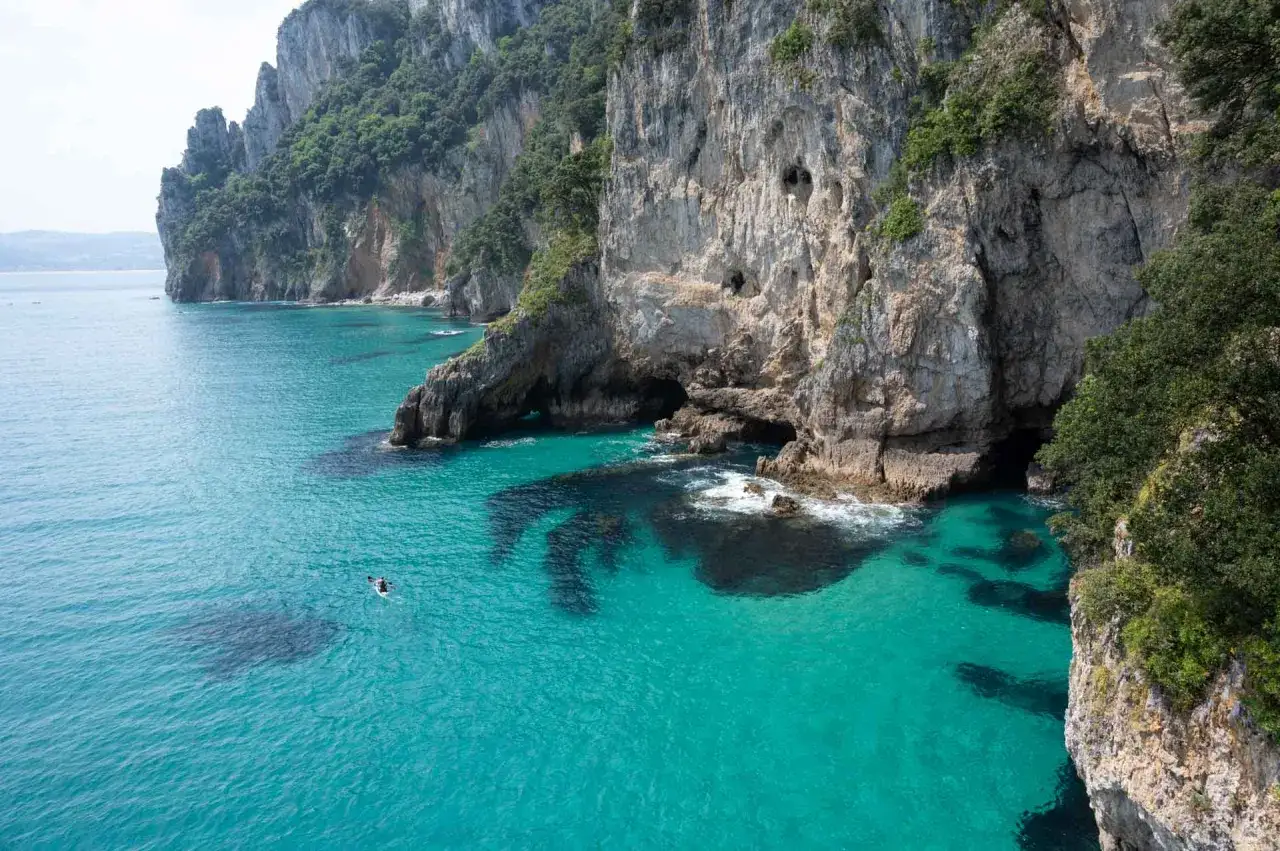 Un kayakista navega cerca de cuevas marinas en acantilados verdes, con aguas turquesas que recuerdan a un **faro de caballo**.