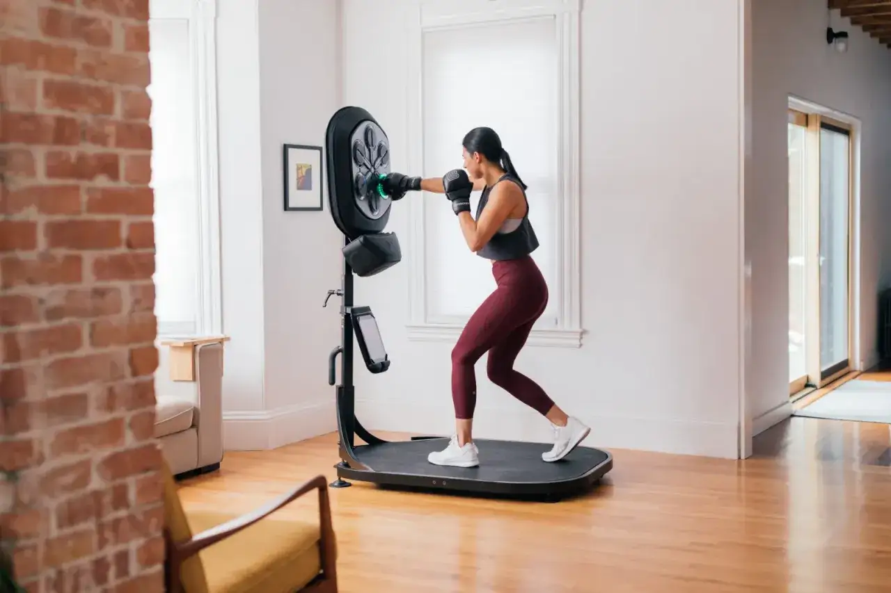 Woman practicing boxing for fitness at home, punching a smart boxing machine.