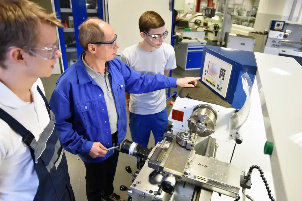 Mistrz pokazuje młodemu czeladnikowi obsługę tokarki CNC.