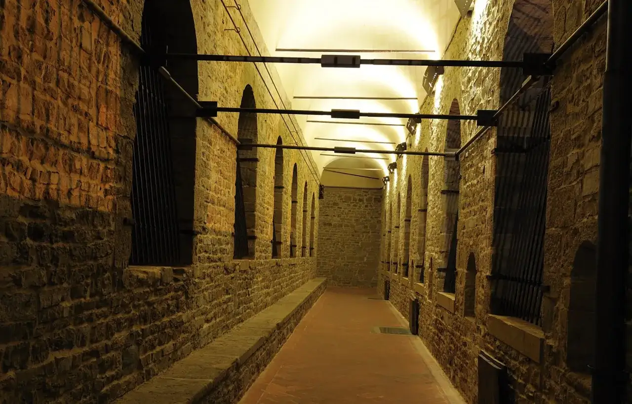 Corridoio con archi e muri in pietra del Palazzo Vecchio, illuminato da luci soffuse.