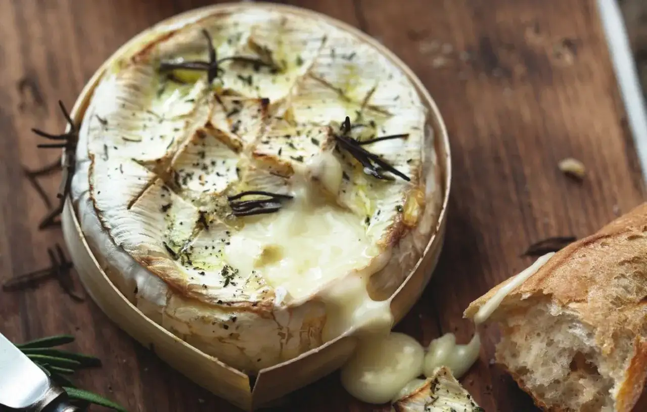 Un camembert au barbecue, fondant et parfumé au romarin, prêt à être dégusté avec une baguette croustillante.