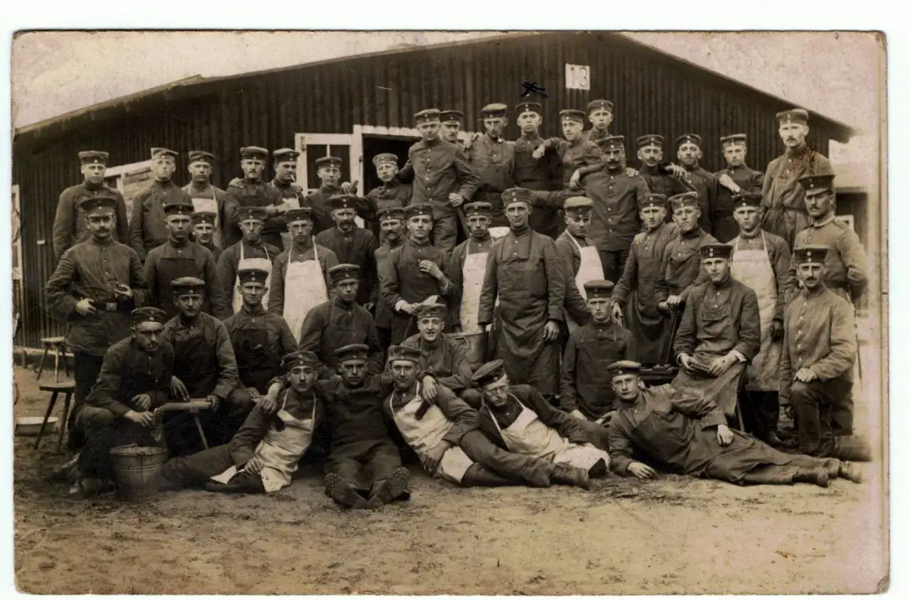 Groupe de soldats en uniforme, possiblement en recherche d'un ancien combattant de la guerre 14-18. Ils posent devant un bâtiment en bois.